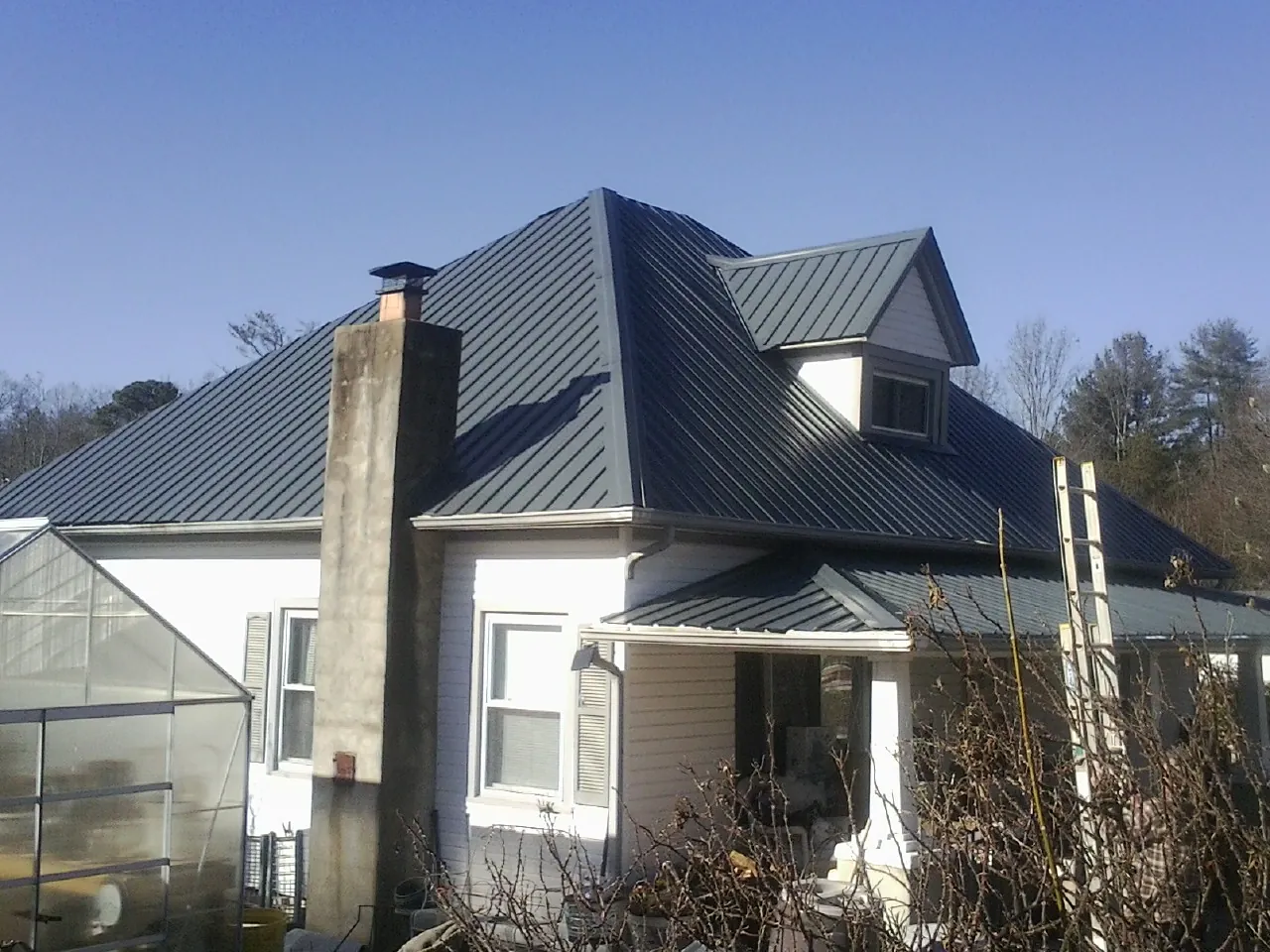 Dark blue standing seam metal roof on a white farmhouse with dormer — Slate & Tile Roof Repair by Roofing Brothers in Lander