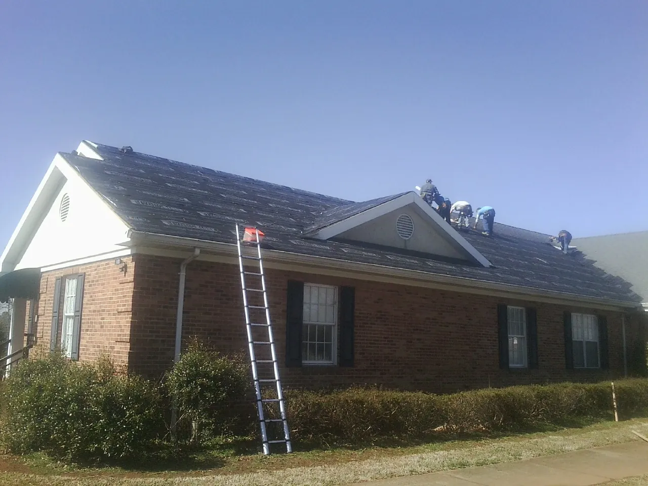 Crew tearing shingles off a brick ranch roof with a ladder set — Emergency Roof Repair work by our crew in Lander