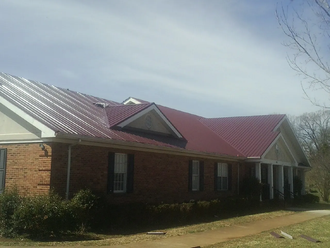 Red metal roof with gabled entries on a long brick building, from a Hail Damage Roof Repair job in Lander