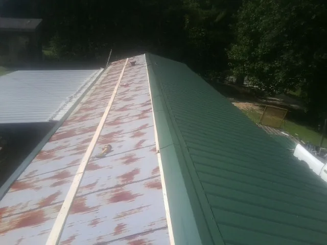 Old rusted panels beside newly installed green metal roofing — Wind Damage Roof Repair by Roofing Brothers in Lander