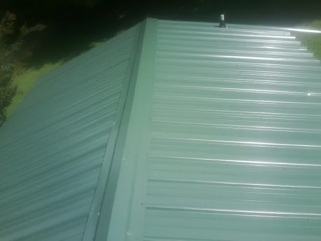 New green metal panels meeting at the ridge of a roof — Flat Roof Repair work by our crew in Lander