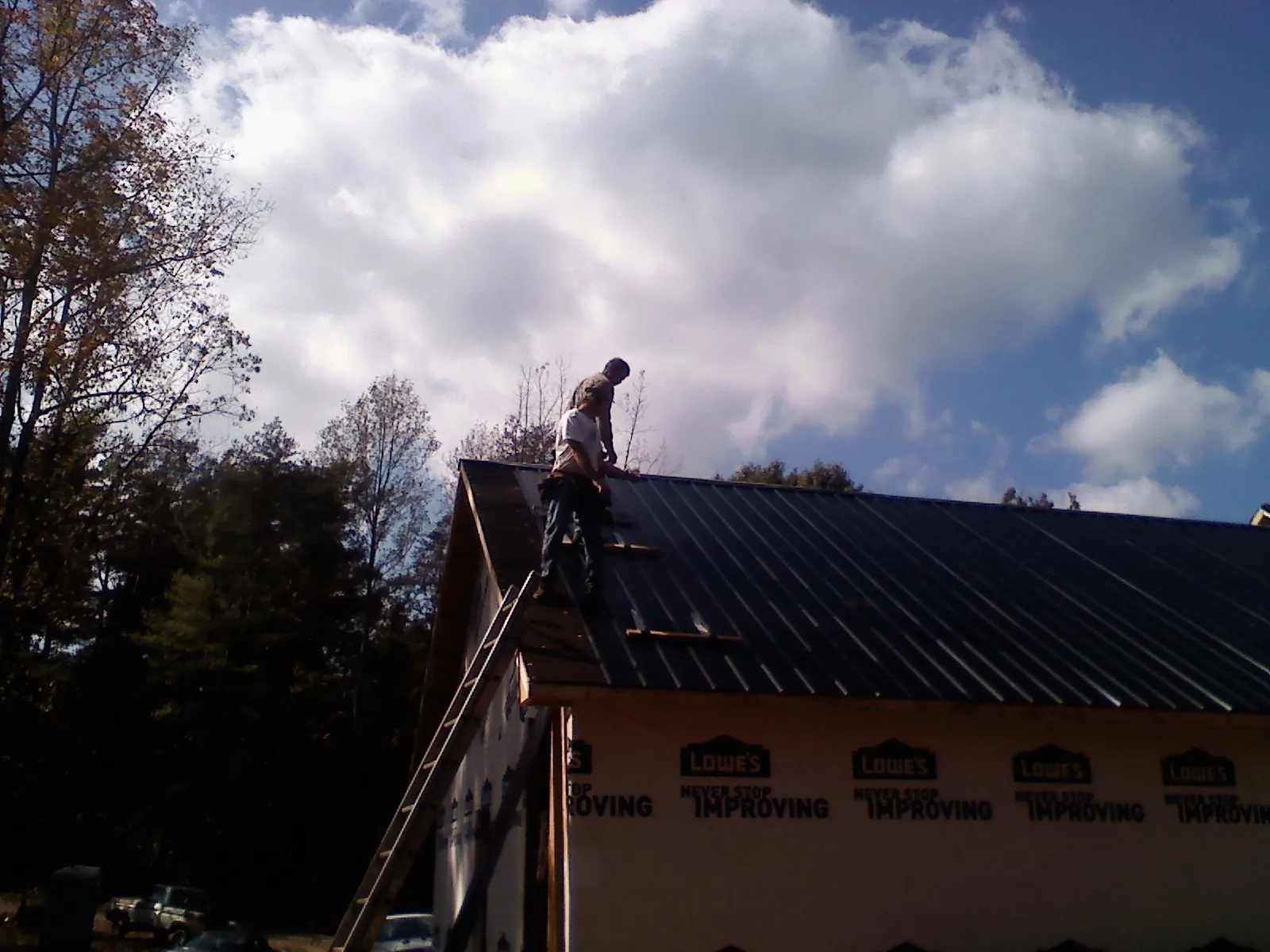Roofer fastening dark metal panels high against a cloudy sky, from a Roof Inspection job in Lander